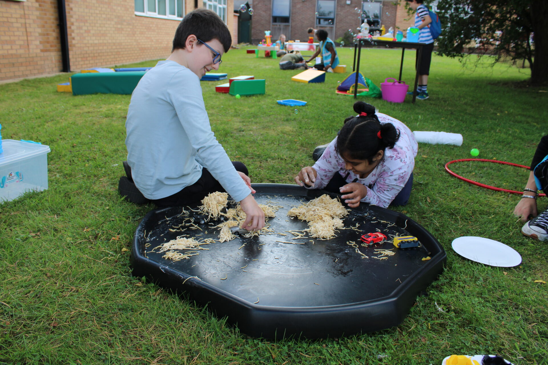 A young boy and girl sitting outside on the grass doing sensory play.